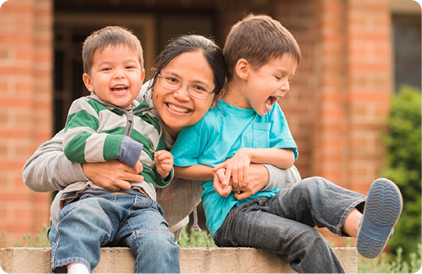 Woman holding two toddlers smiling in front of home