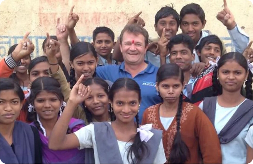 Man standing in the middle of a group of Indian children, all smiling